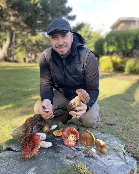 Colin Disheroon kneeling beside a stump with freshly picked boletes and other wild mushrooms