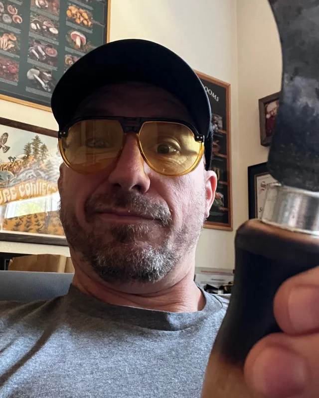 Colin in amber glasses grinning at the camera and holding up his curved mushroom knife